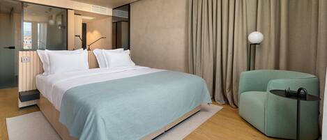 A modern hotel room with a large bed, a seating area, and a view through a glass door.
