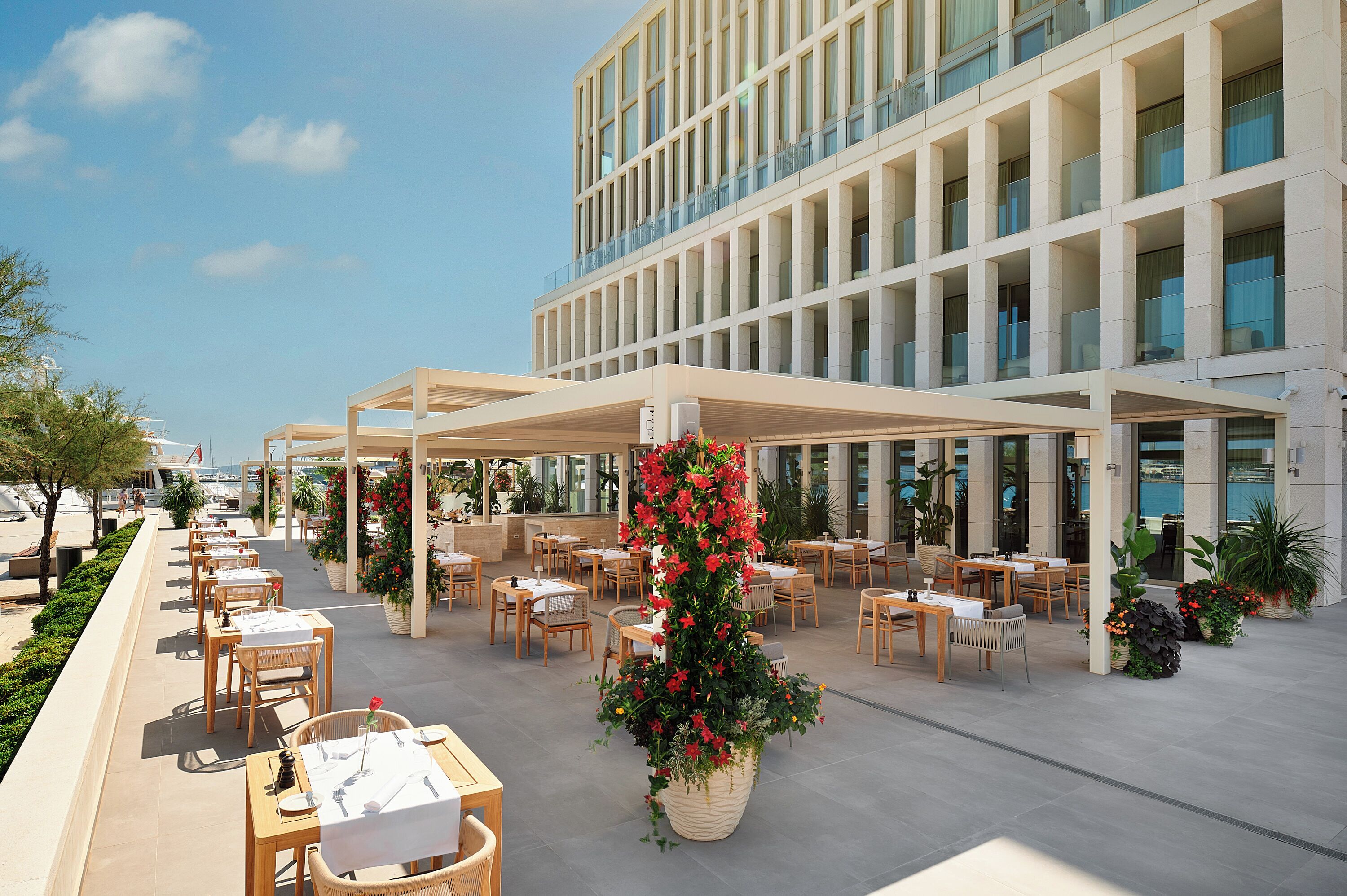 An outdoor dining area with tables and chairs, surrounded by potted plants and a large flower arrangement.