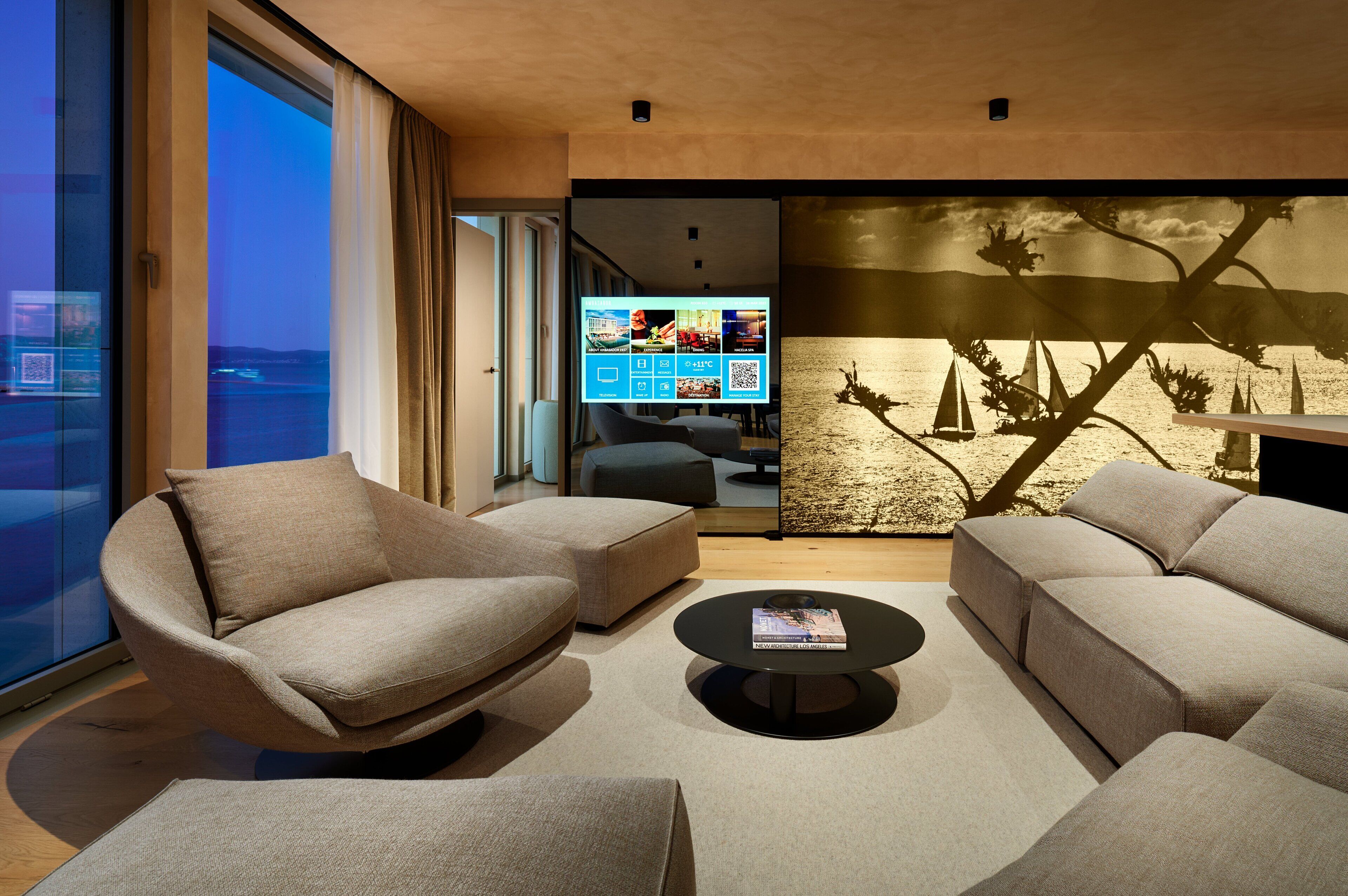 A modern living room with a large TV, comfortable seating, and a scenic view through the window.