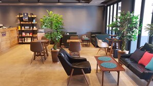 Un moderno vestíbulo de hotel con áreas de descanso, un mostrador de recepción y grandes ventanales.