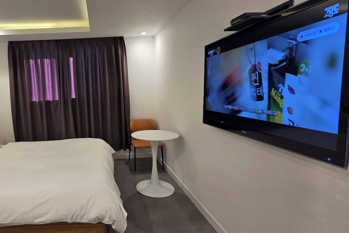 A hotel room with a bed, a small table, a TV, and a curtain.