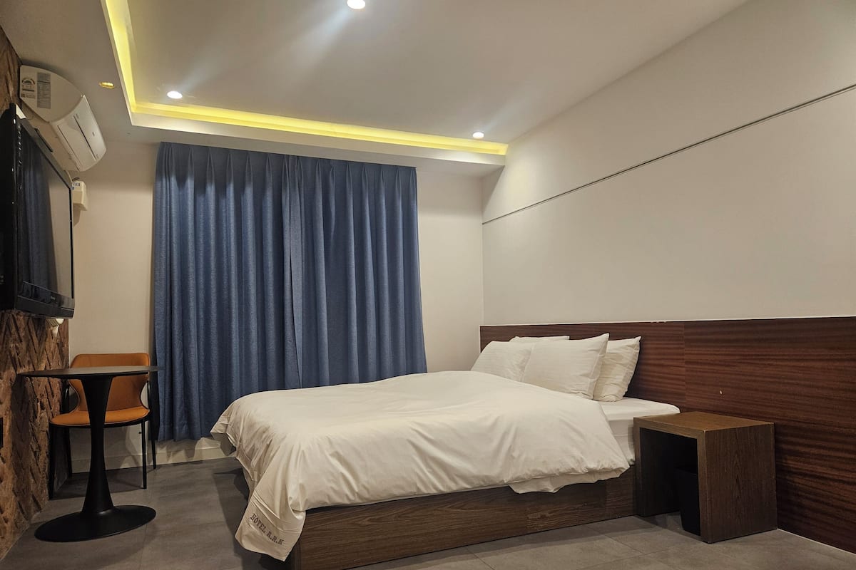 A modern hotel room with a bed, bedside table, and a desk with a chair.