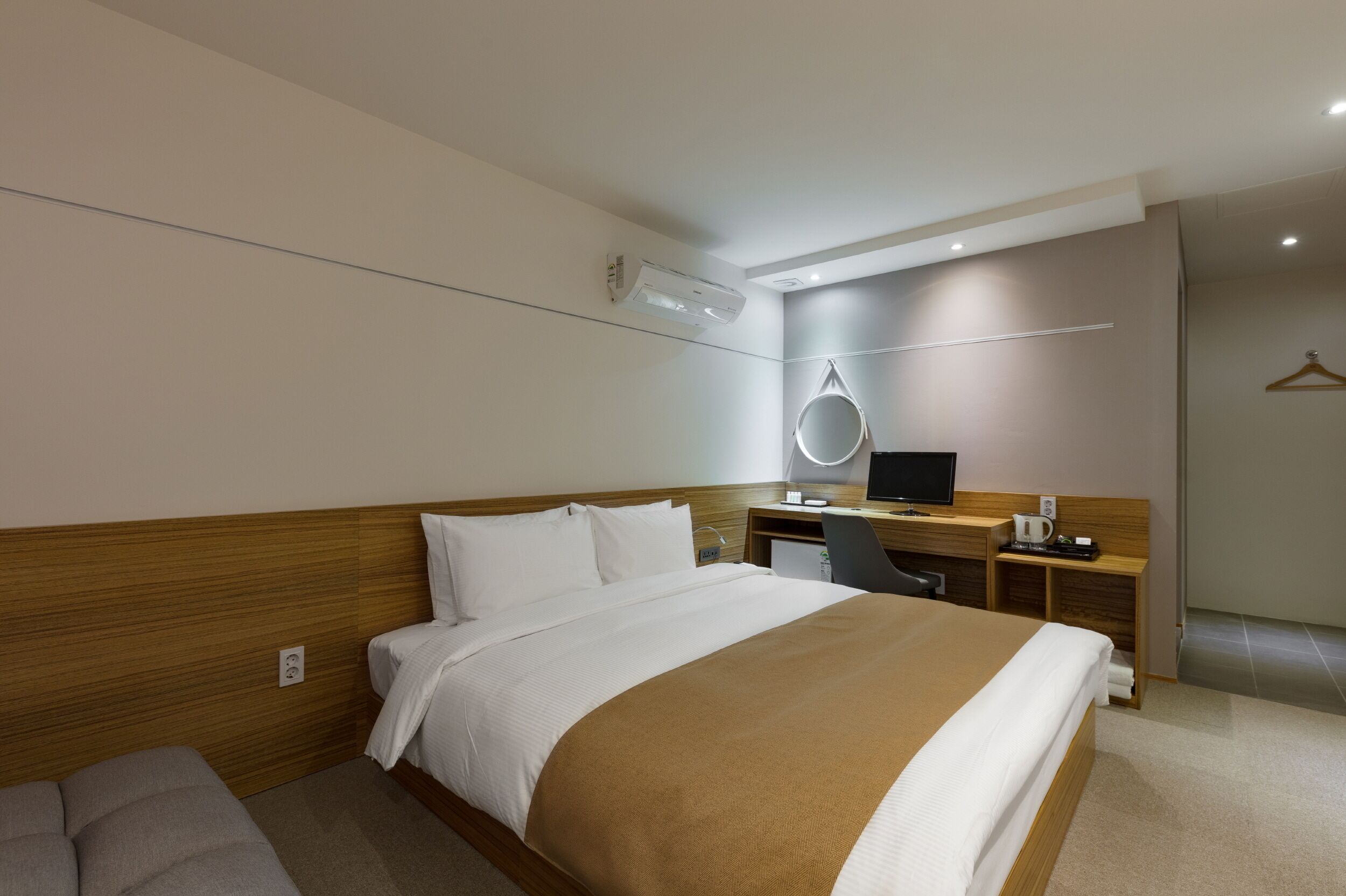 A modern hotel room with a large bed, a desk with a computer, a chair, and a small TV.