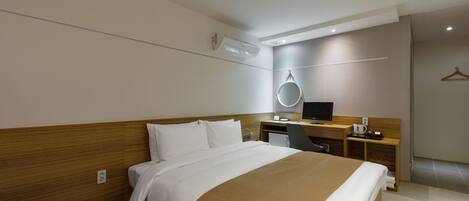 A modern hotel room with a large bed, a desk with a computer, a chair, and a small TV.