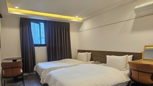 Habitación de hotel con dos camas, una mesita, sillas, una ventana con cortinas y un equipo de aire acondicionado.