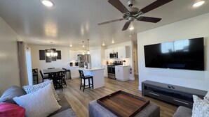 A modern living room with a large flat-screen TV, grey sofas, a wooden coffee table, and a ceiling fan. - Near Zion NP I Dark Skies I Garage & Trailer Parking (Kanab)