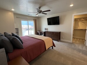 A bedroom with a bed, a desk, a TV, a ceiling fan, and a closet.