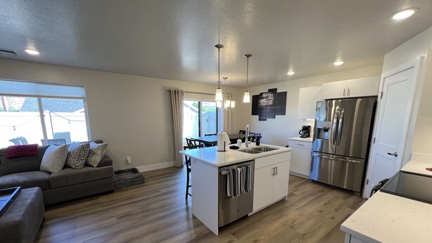 A modern kitchen with a central island, stainless steel appliances, and a dining area with a sofa and chairs. - Near Zion NP I Dark Skies I Garage & Trailer Parking (Kanab)