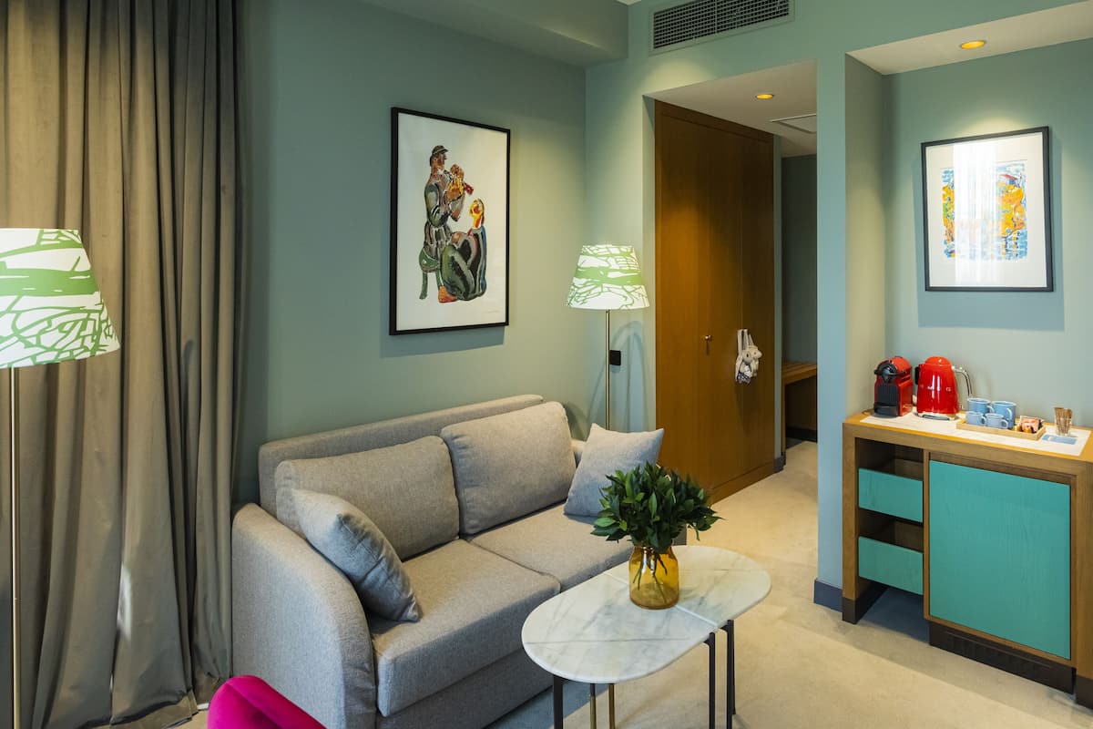 Un salon moderne avec un canapé gris, une petite table blanche ornée d’un vase et un meuble turquoise abritant une machine à café.