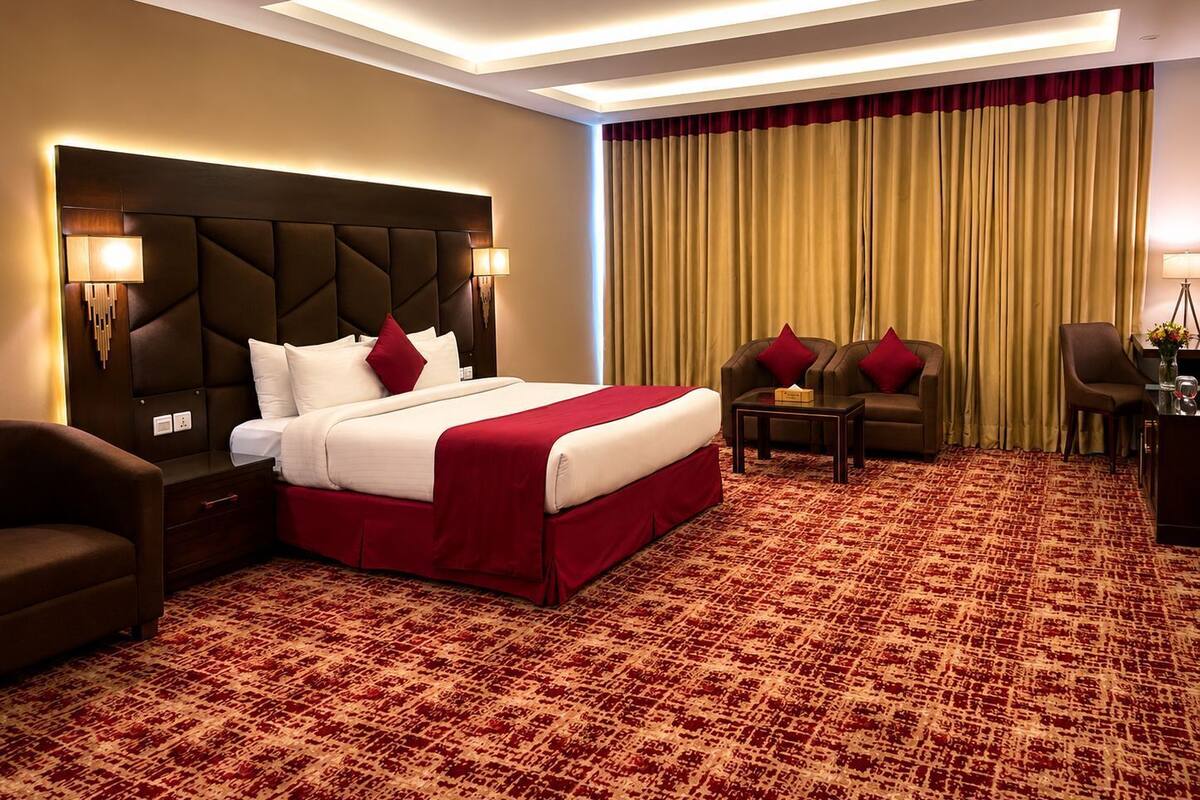 A hotel room with a large bed, two armchairs, a small table, and a desk with a lamp.