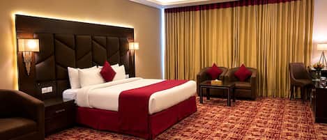 Habitación de hotel con una cama grande, dos sillones, una mesita pequeña y un escritorio con una lámpara.