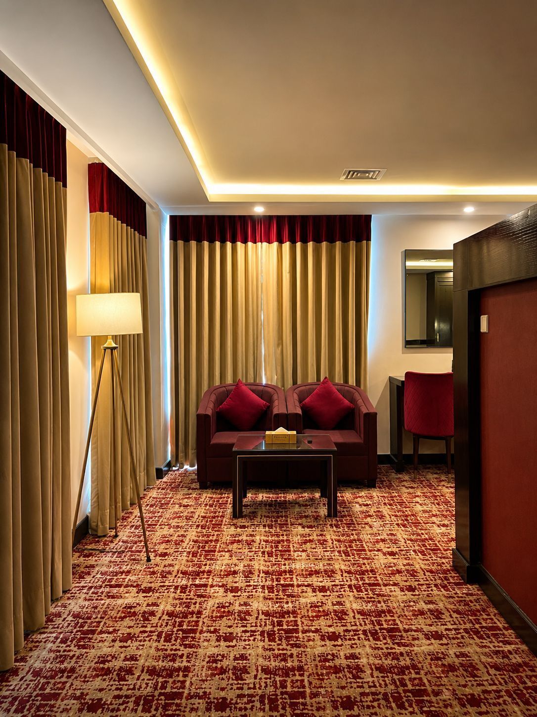 Habitación de hotel con sofá, una mesa de centro, lámpara y una silla roja.