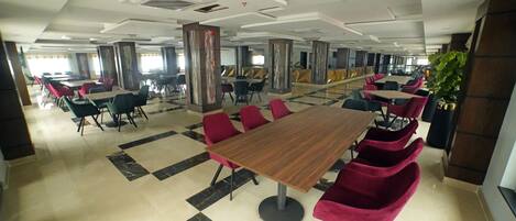 A spacious dining area with multiple tables and chairs, large pillars, and a tiled floor.