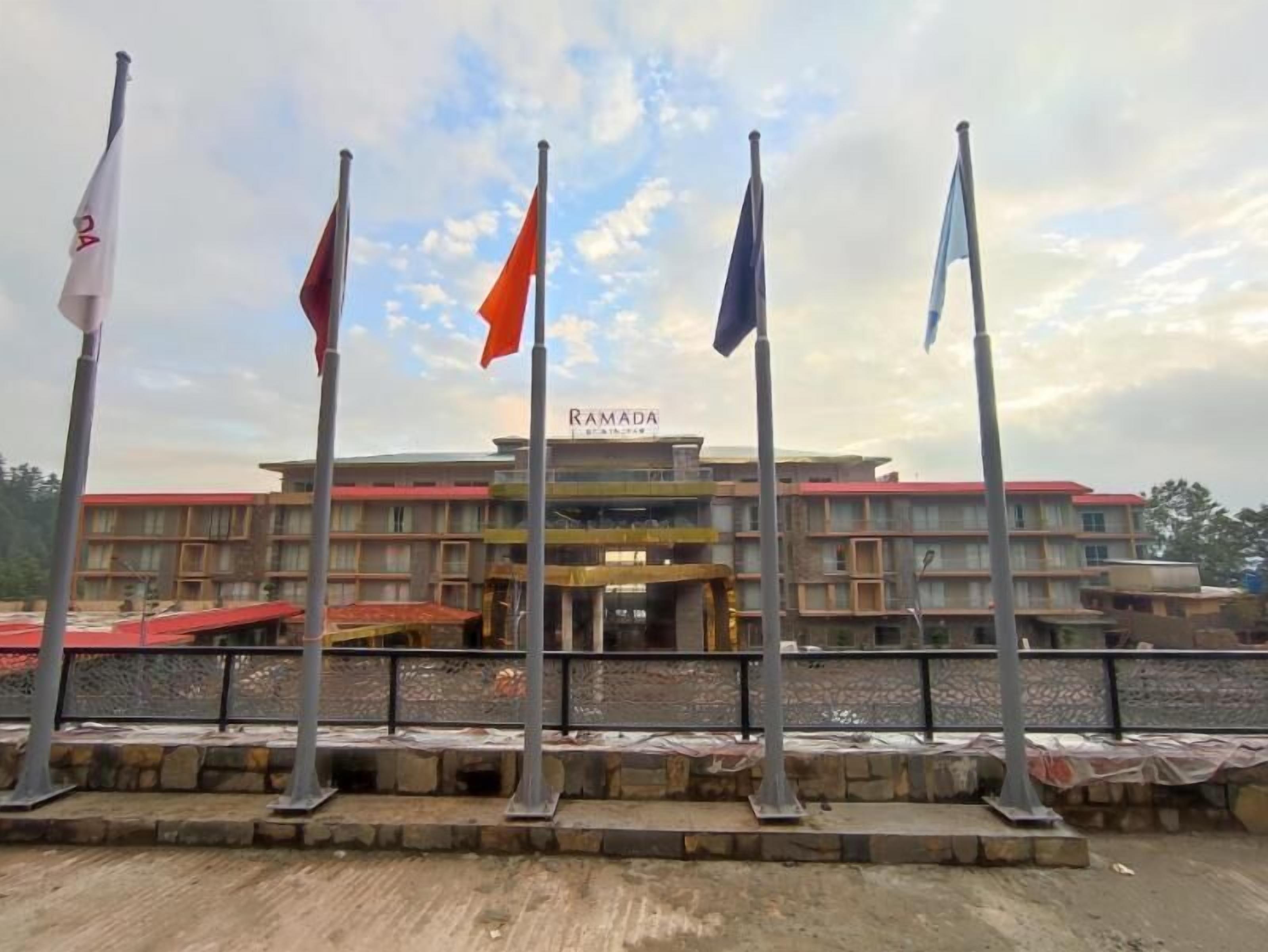 A hotel with a sign reading 'RAMADA' and multiple flags in front.