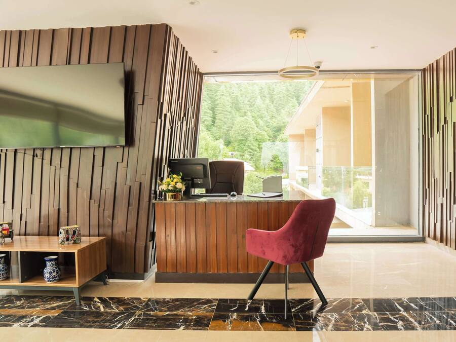 A modern reception area with a wooden panel wall, a flat-screen TV, a desk with a computer, and a red chair.