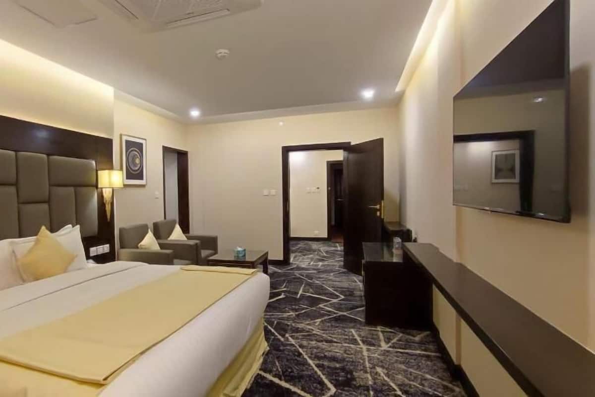 A hotel room with a bed, a desk, a chair, a TV, and a door leading to another room.