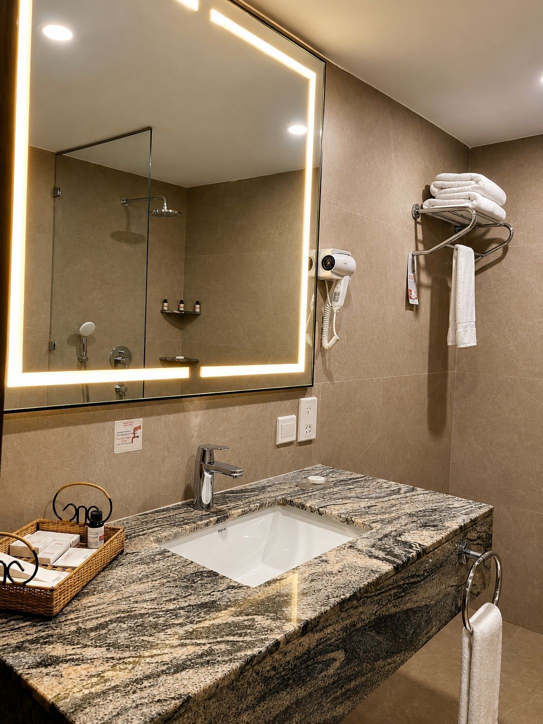 Un baño con un espejo grande, un lavabo, una ducha, un secador de pelo y un perchero para toallas.