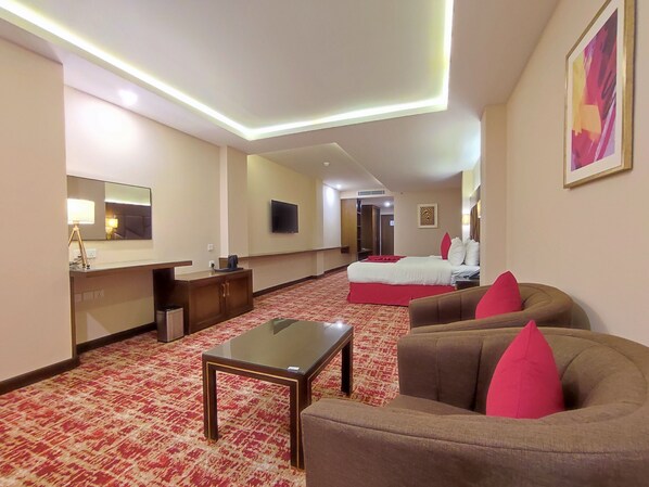 A hotel room with a bed, a sofa, a coffee table, a desk, a TV, and a mirror. - Ramada by Wyndham Murree Lower Topa Resort (Murree)