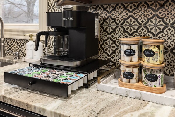 Una cafetera, un cajón para cápsulas de café y tarros de crema para café sobre una encimera de cocina.