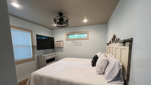 Ein Schlafzimmer mit Bett, Fernseher, Fenster und Deckenventilator.