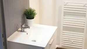Un bany amb un rentapeus blanc, una petita planta en test, un mirall i un radiador blanc.