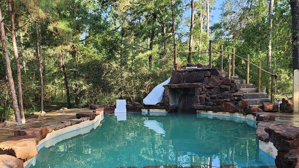 Una piscina natural con cascada, rodeada de árboles y terreno rocoso.