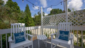 Une terrasse en bois avec deux fauteuils à bascule et une petite table, chacun agrémenté d’un coussin portant l’inscription « The Scotsman Porch ».