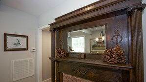 Une cheminée surmontée d’un miroir, encadrée de pommes de pin et agrémentée d’un tableau encadré au mur.