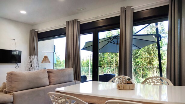 Una sala de estar moderna con un sofá, una mesa de comedor y sillas. Hay un televisor montado en la pared, y una ventana con cortinas.