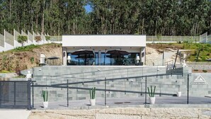 Un edificio moderno con techo plano, amplios ventanales y un acceso pavimentado con cerramiento de metal.