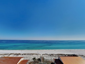 Blick auf einen Strand mit blauem Himmel, Sand und Häusern mit roten Dächern.