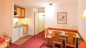 Ein kompaktes Hotelzimmer mit Küchenzeile, einem Essbereich mit Holzkreisen, einem kleinen Tisch und einem gerahmten Bild an der Wand.