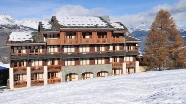 Ein mehrstöckiges Hotel mit Balkonen vor einer verschneiten Bergkulisse.