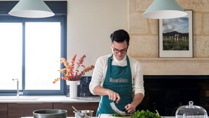 A modern kitchen with a chef preparing food, wooden cabinets, a large window, and a decorative vase with autumn leaves. - Maison Groleau (Mombrier)
