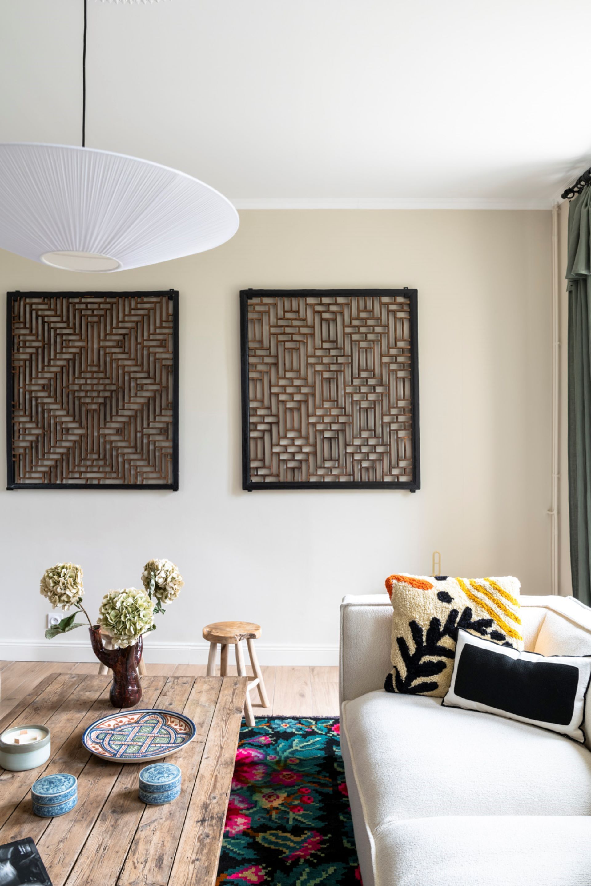 A modern living room with a sofa, decorative pillows, a wooden coffee table with a vase and plates, and two wall-mounted woven art pieces.