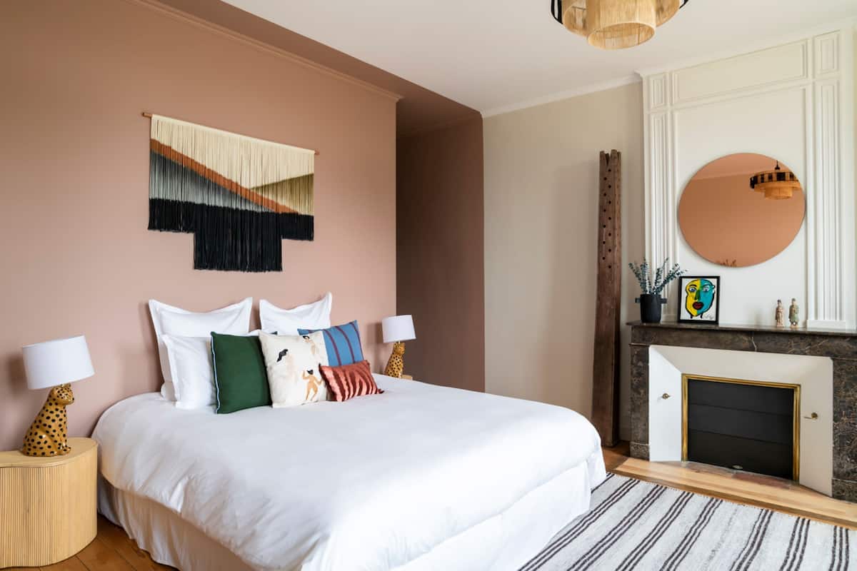 A bedroom with a large bed, a fireplace, and a wall-mounted mirror.