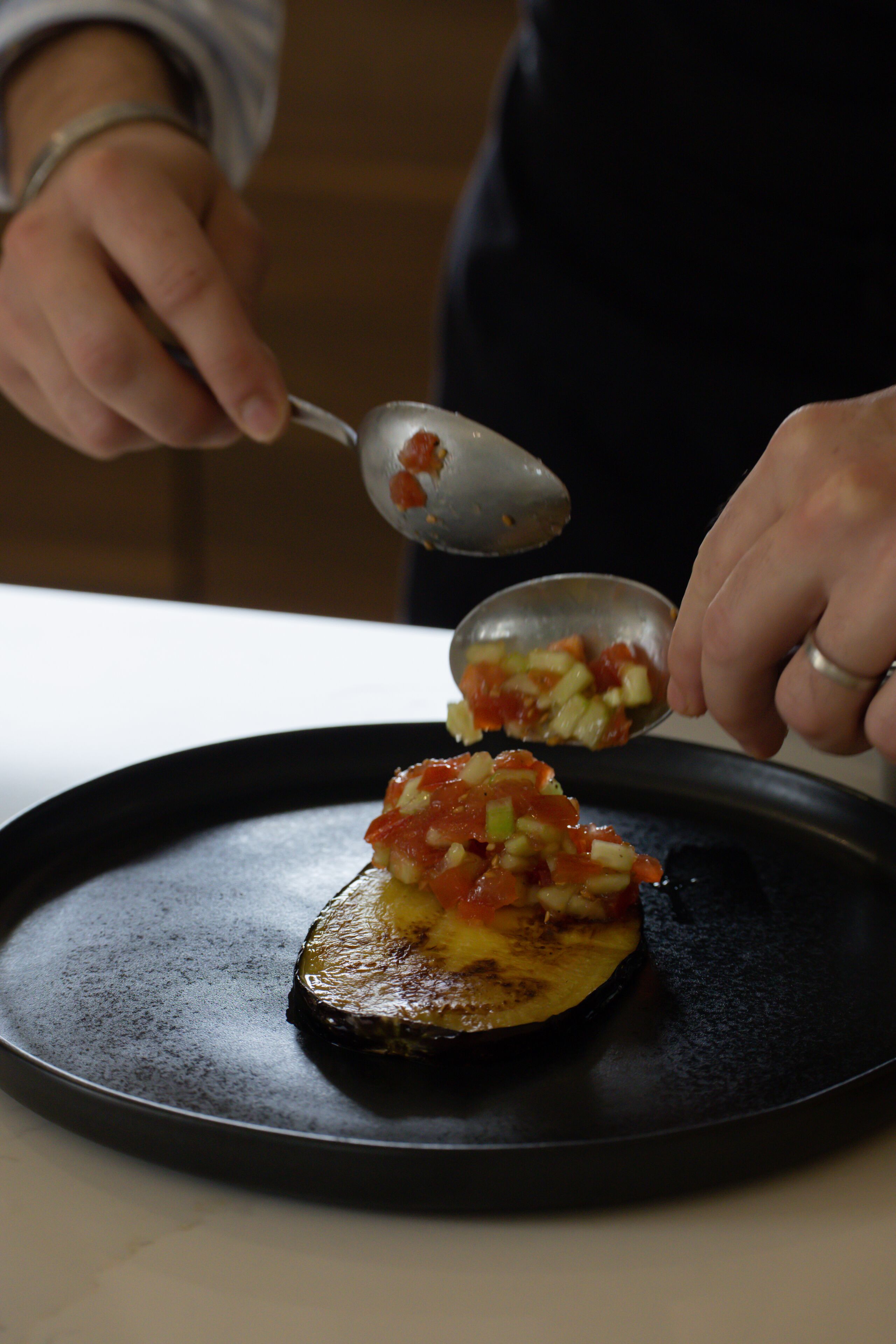 A person cooking on a stove with a pan on a black plate.