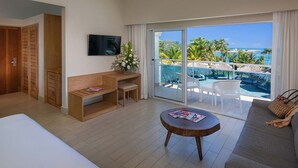 A hotel room with a balcony, a bed, a TV, a small table, and a sofa. - Luxurious 1 Bedroom Tropical Junior Suite (Dominican Republic)