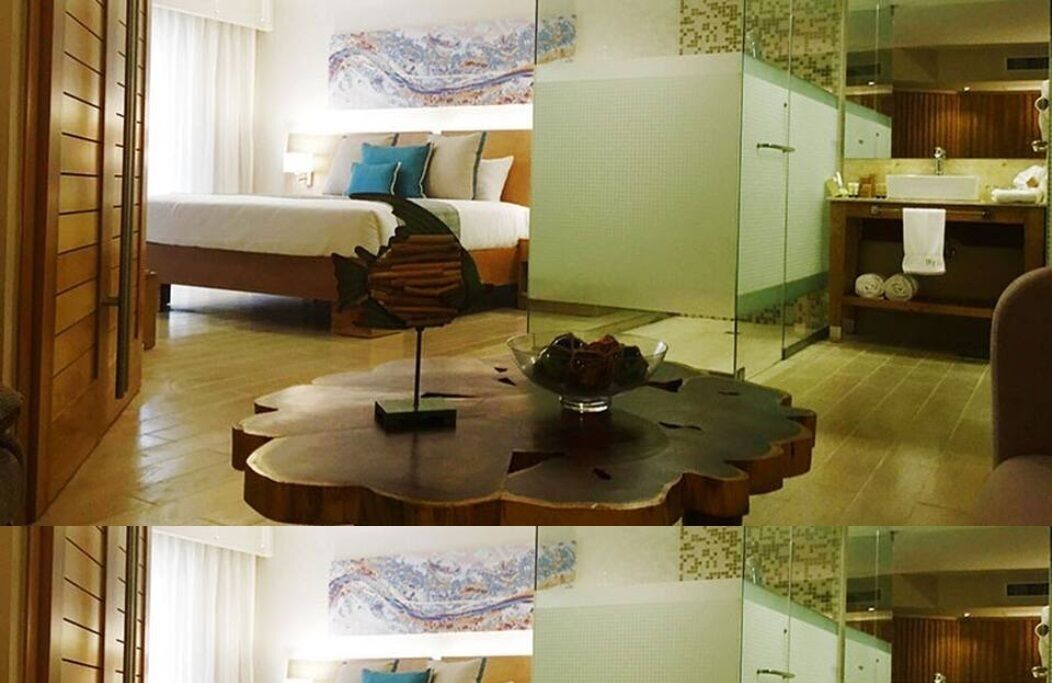 A hotel room with a bed, a wooden coffee table, and a bathroom with a sink and mirror.