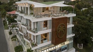 A multi-story hotel with a rooftop terrace, large windows, and a prominent logo on the facade.