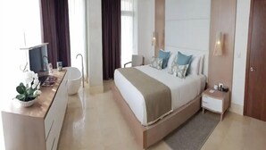 A modern hotel room with a large bed, bedside tables, a desk with a chair, a large window, and a bathroom.