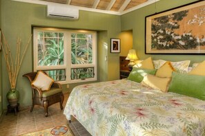 A bedroom with a bed, a window with a view of greenery, a chair, and a lamp.