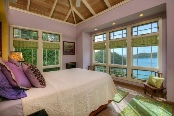 A bedroom with a large bed, multiple windows, and a view of the outdoors.