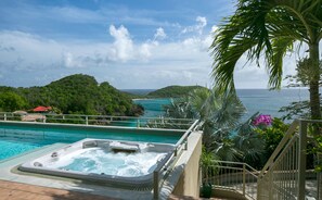 A hot tub by a pool with a view of the ocean and a mountainous landscape.