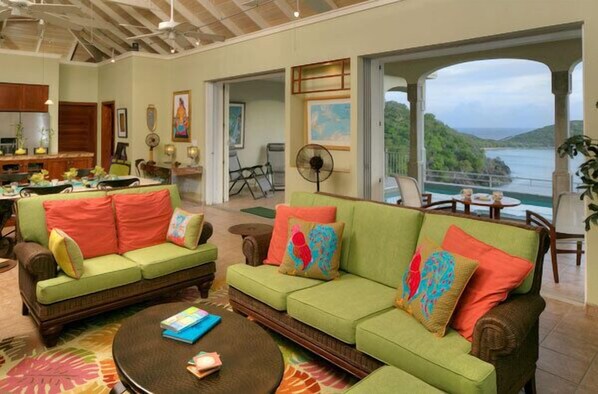 A spacious living area with a green sofa set, a coffee table, and a view of a body of water through large windows.