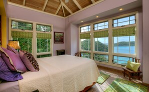 Une chambre à coucher avec un grand lit, de nombreuses fenêtres ornées de rideaux verts et une vue sur un paysage naturel.