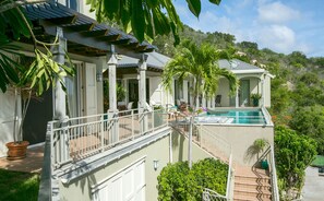 Une maison à deux étages avec une piscine, du mobilier d’extérieur et une végétation luxuriante.