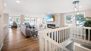 Un salon spacieux avec une cheminée, un coin repas et un balcon doté d’une balustrade blanche.