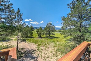 A wooden deck overlooking a grassy area with trees and a clear sky. - Mountainside Tree House Retreat (Larkspur)