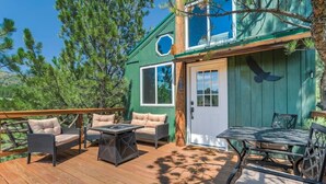 A wooden deck with outdoor furniture, a door with a bird silhouette, and a view of pine trees. - Mountainside Tree House Retreat (Larkspur)